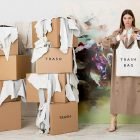 nainen poseeraa pahvilaatikoiden ja laukkumateriaalin keskellä